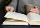 A person holding a coffee cup and reading an open book.