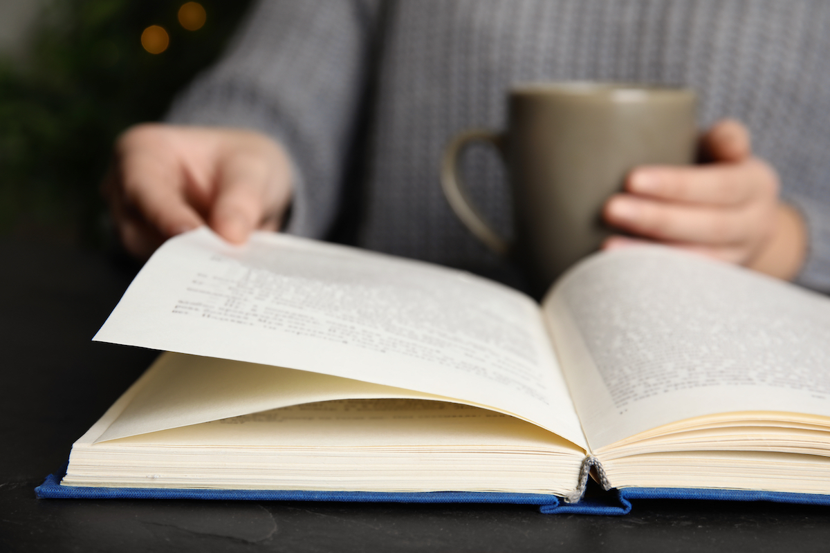 A person holding a coffee cup and reading an open book.