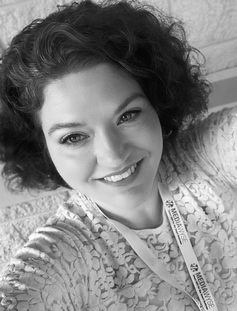 A black-and-white image of Danielle Dahl. A female with short, dark, curly, hair and blue eyes. She is wearing a lacey top.