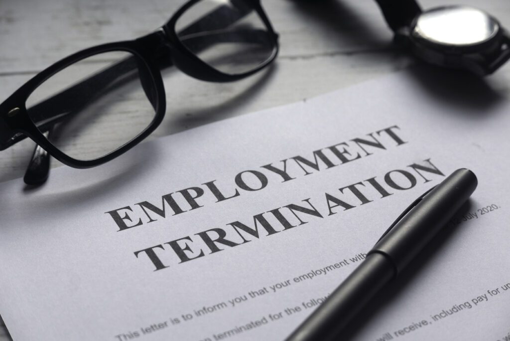 A document with bold lettering that reads 'Employment Termination.' A pair of glasses and a pen sit next to it.
