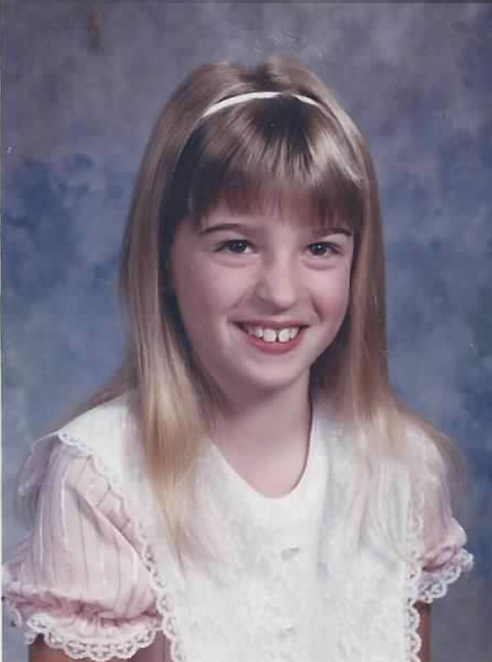 A picture of the author from childhood. A little blonde girl against a blue backdrop.