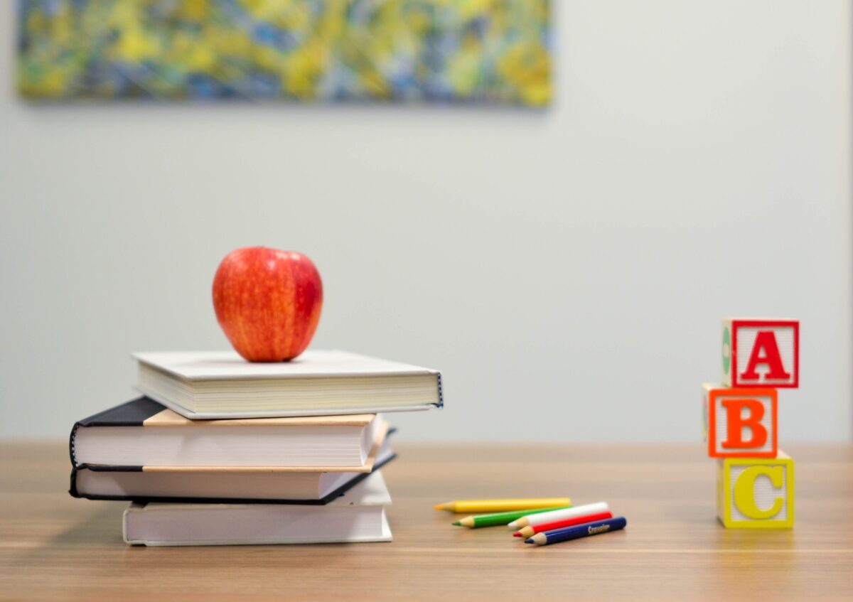 A few books on a teacher's desk with an apple on top of them. There are also ABC blocks and colored pencils on the desk.