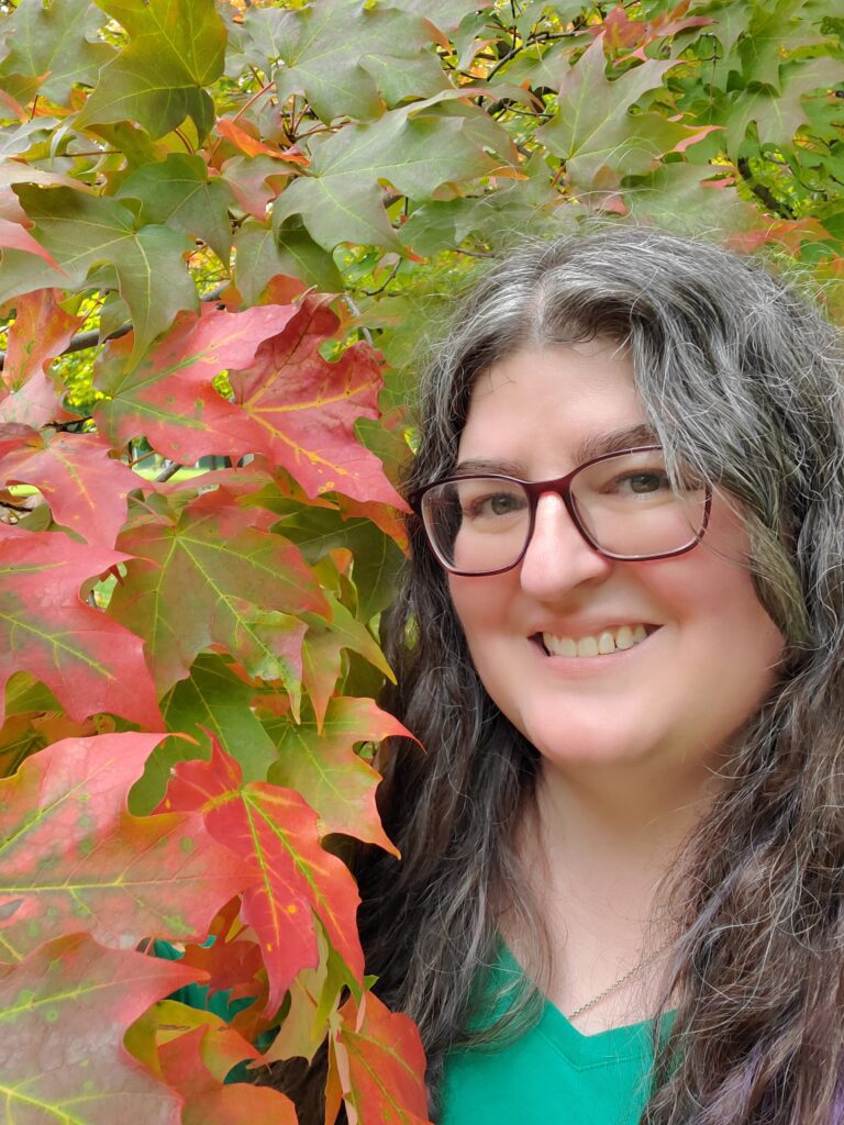 A photo of the author next to red and green foliage.