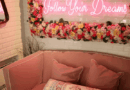 A mirror surrounded by flowers with a neon light that says follow your dreams hangs on an ivory colored wall. There is a pink couch.