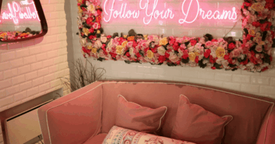 A mirror surrounded by flowers with a neon light that says follow your dreams hangs on an ivory colored wall. There is a pink couch.