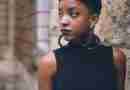 Black Woman with earrings standing next to stone wall looking away