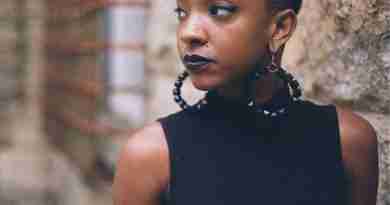 Black Woman with earrings standing next to stone wall looking away
