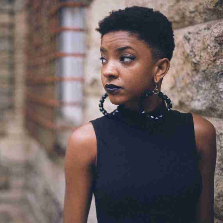 Black Woman with earrings standing next to stone wall looking away