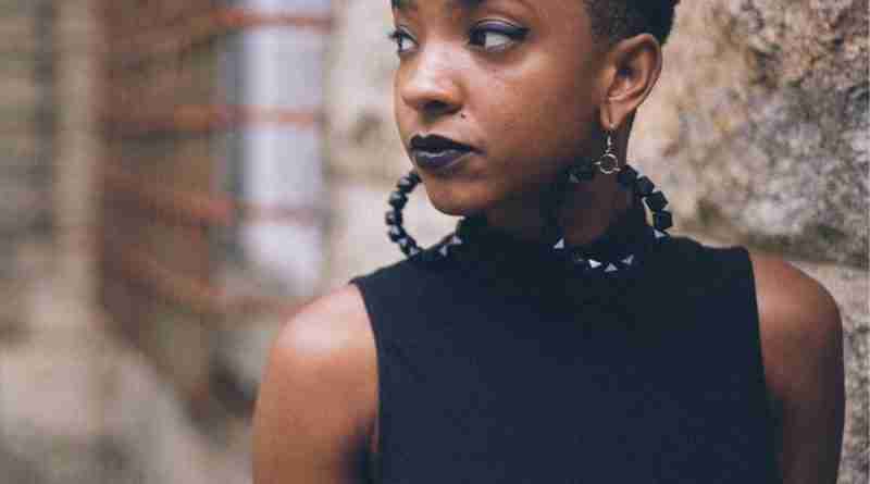 Black Woman with earrings standing next to stone wall looking away