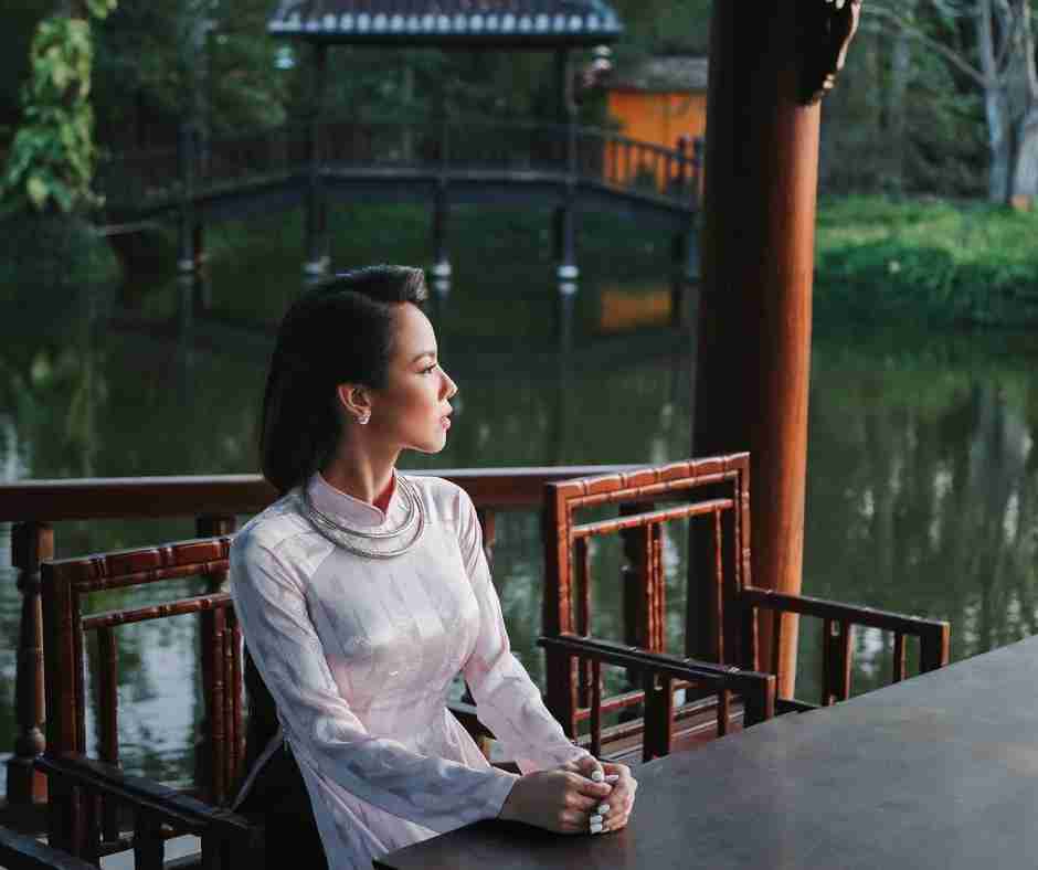 Untitled design (18) - Resilient Stories Pretty Asian woman sitting by a lake in quiet contemplation