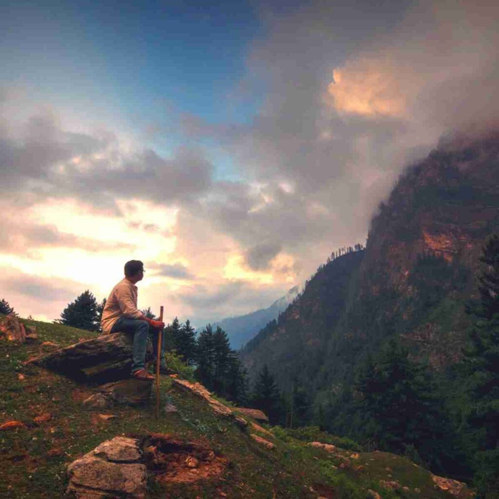 Man sitting on a mountainside looking at a clouds covering the adjacent mountain. Photo by Arijit Chakraborty from Pixabay