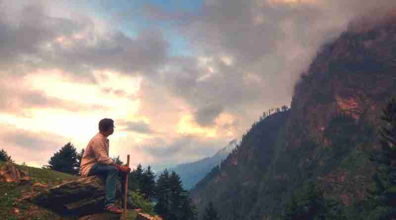 Man sitting on a mountainside looking at a clouds covering the adjacent mountain. Photo by Arijit Chakraborty from Pixabay