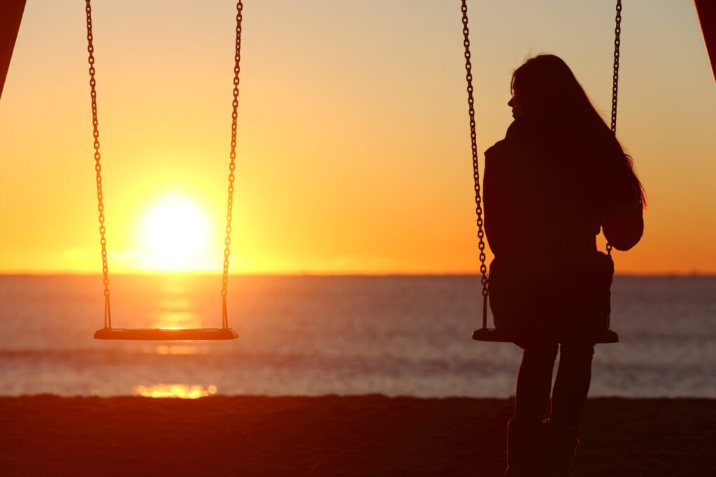 Sad girl on swings alone at sunset. 