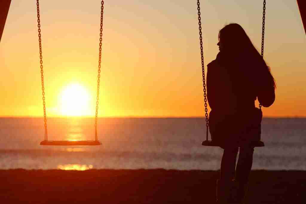 Sad girl on swings alone at sunset. 