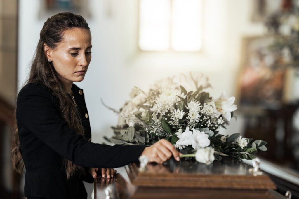 Funeral, sad and woman with flower on coffin after being orphaned. Grief, death and young female putting a rose on casket in church with sadness, depression and mourning