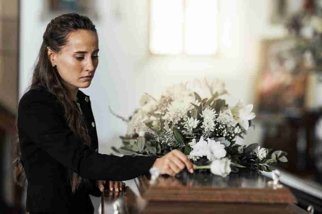 Funeral, sad and woman with flower on coffin after loss of a loved one, family or friend. Grief, death and young female putting a rose on casket in church with sadness, depression and mourning - Resilient Stories Funeral, sad and woman with flower on coffin after being orphaned. Grief, death and young female putting a rose on casket in church with sadness, depression and mourning
