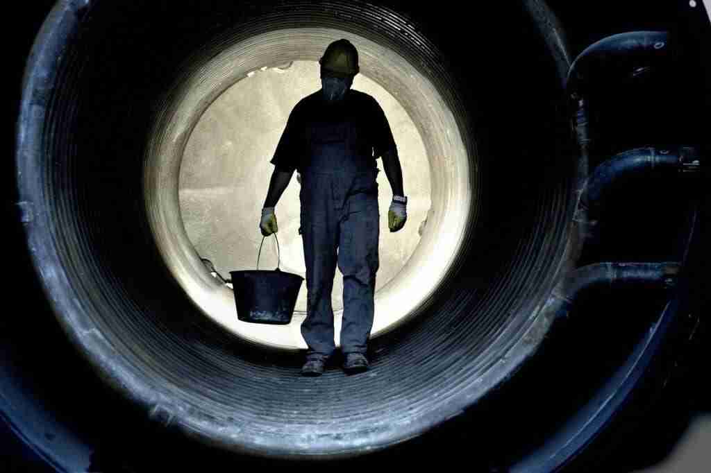 Worker with mask in large steel tube carrying heavy bucket illustrating grit. grit quotes.