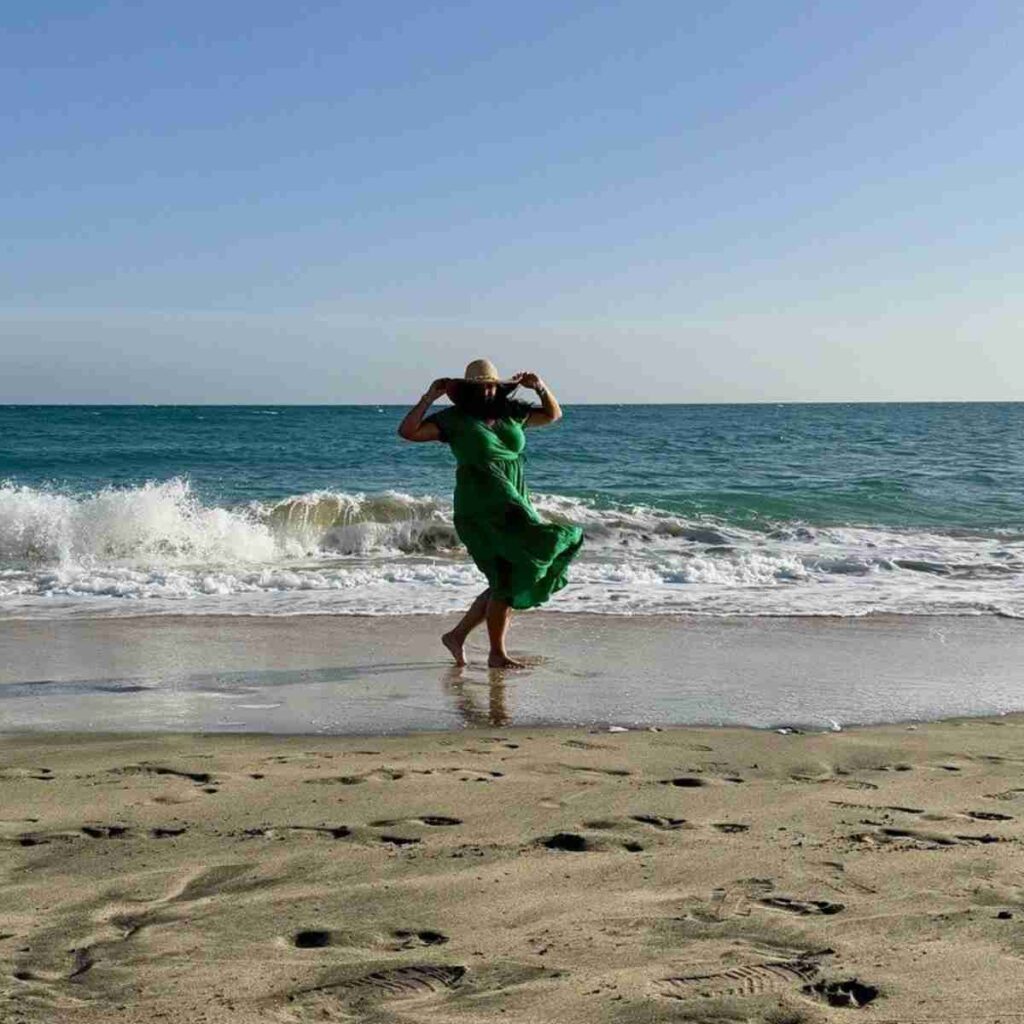 Woman in green dress on beach with hat wind blowing hair and dress. Image by Myléne from Pixabay