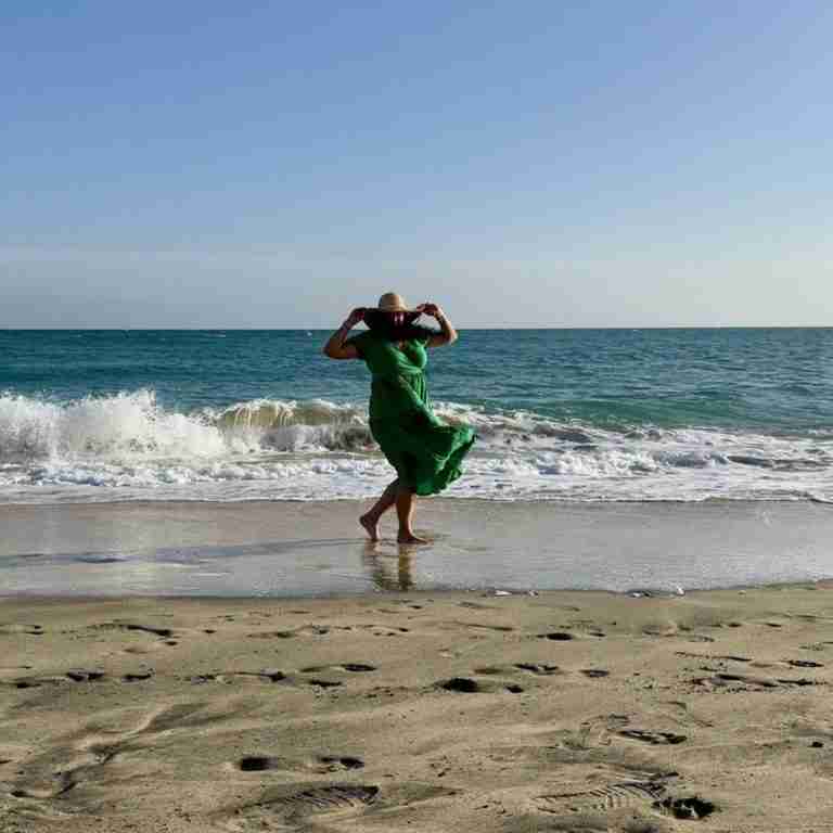 Woman in green dress on beach with hat wind blowing hair and dress. Image by Myléne from Pixabay
