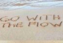 Ocean beach with "go with the flow" written in sand