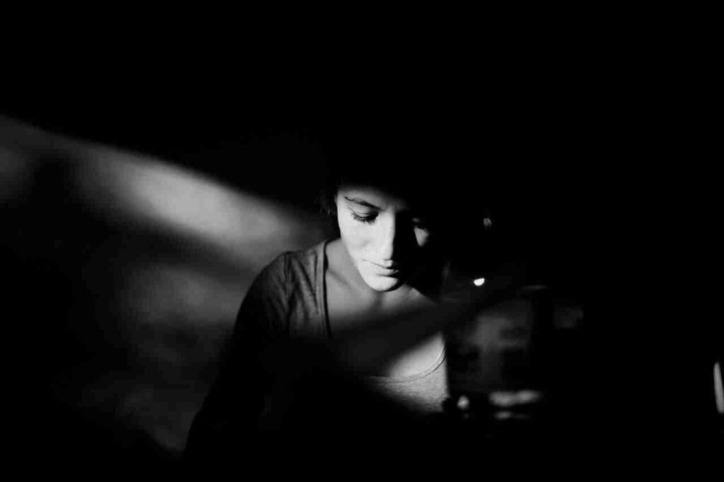 Black and white photo of woman in dark room, looking sad, with light from window hitting her face