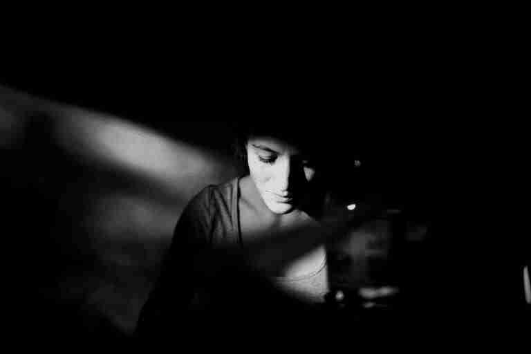 Black and white photo of woman in dark room, looking sad, with light from window hitting her face