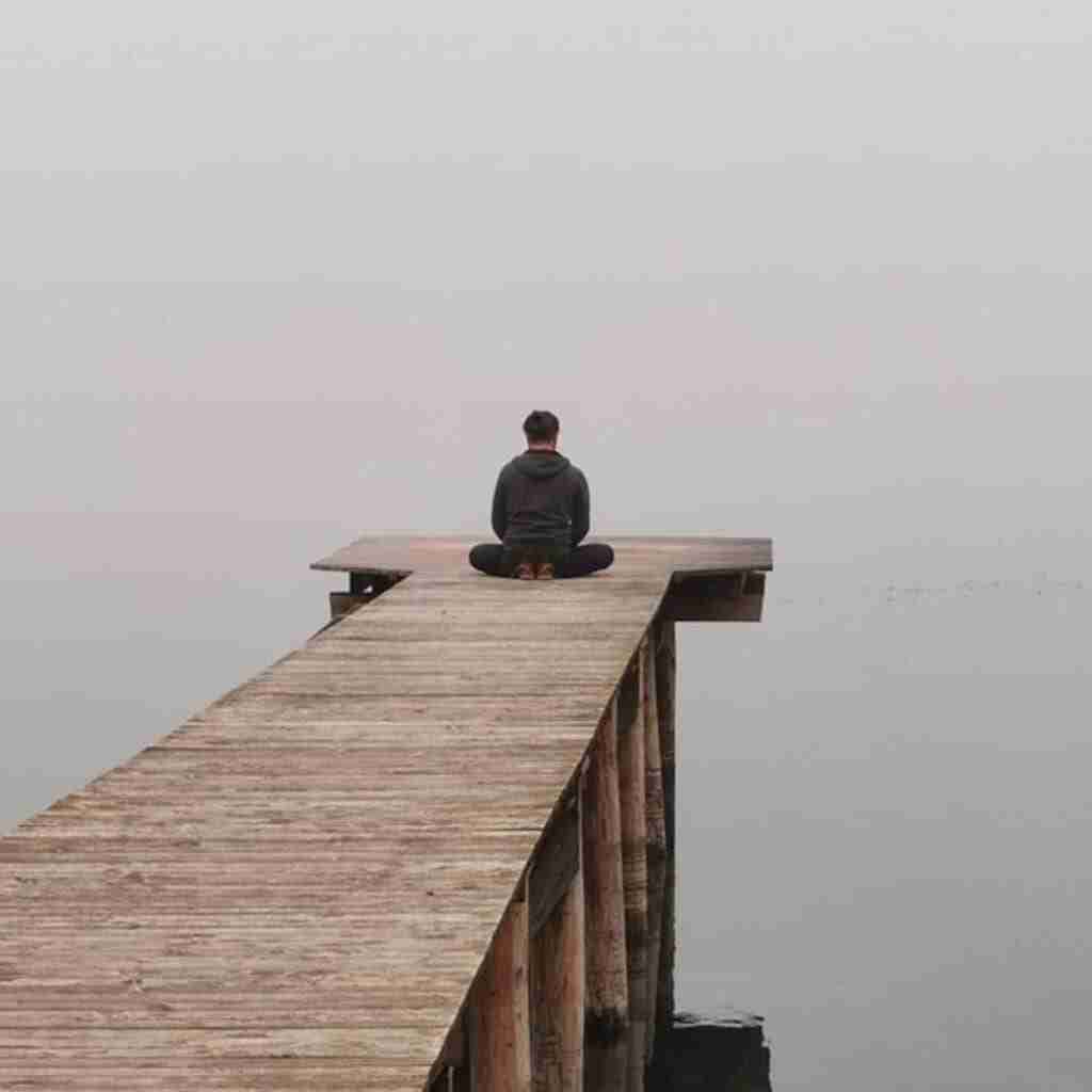 3 - Resilient Stories Man sitting on a dock meditating in front of serene foggy lake