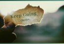 A person holding a little slip of paper that says "keep going quotes" in front of a mountain background.