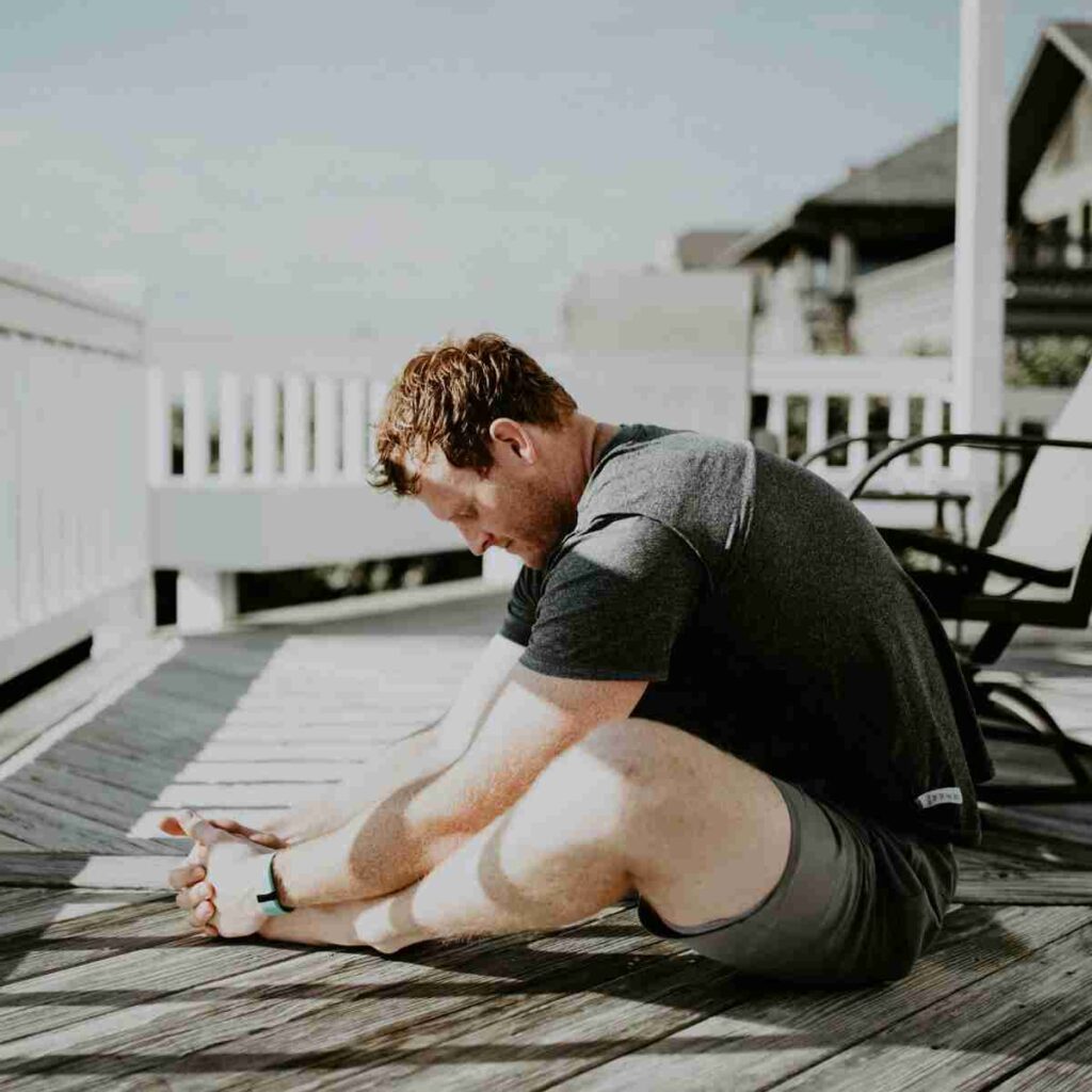 Man doing yoga on porch in sunlight. Photo by Scott Broome on Unsplash