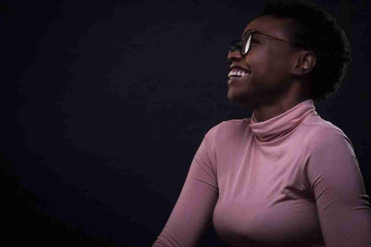 Profile of an African American woman wearing a pink turtleneck and dark-rimmed glasses smiling/laughing