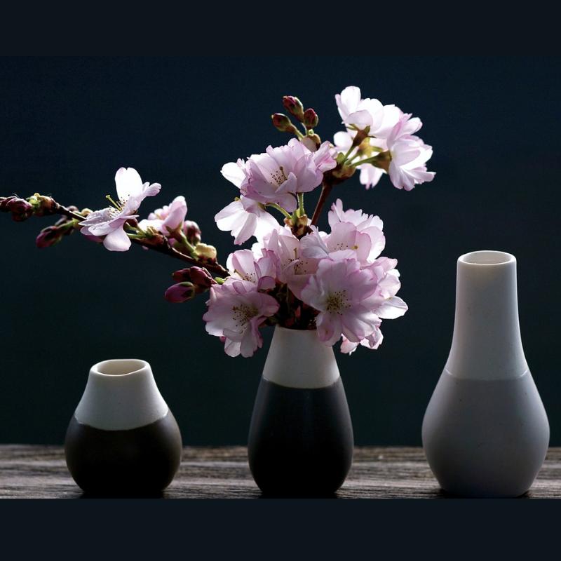 Three different ceramic vases in a line with cherry blossoms in the middle vase  depicting an Ikebana flower arrangement. 