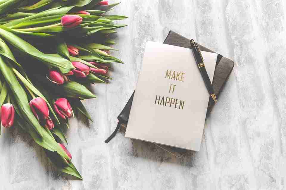 Bouquet of red tulips next to a day planner with a note that says "Make it Happen" and a pen sitting on top of it.