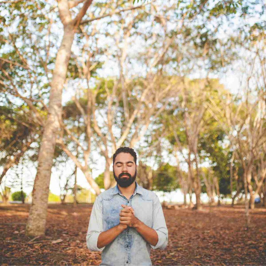 Man standing in sunlight woods praying. Photo by Naassom Azevedo on Unsplash