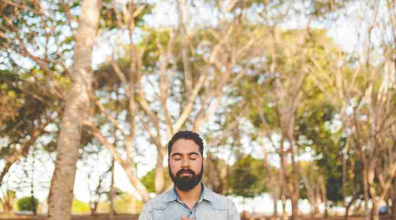 Man standing in sunlight woods praying. Photo by Naassom Azevedo on Unsplash