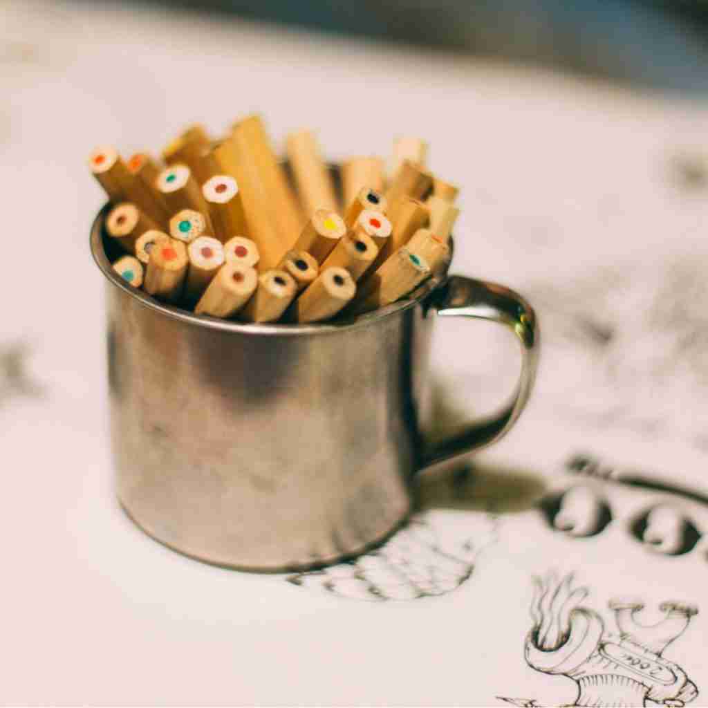 Untitled design (58) - Resilient Stories Photo of colored pencils in a metal cup, sitting on top of images ready for coloring