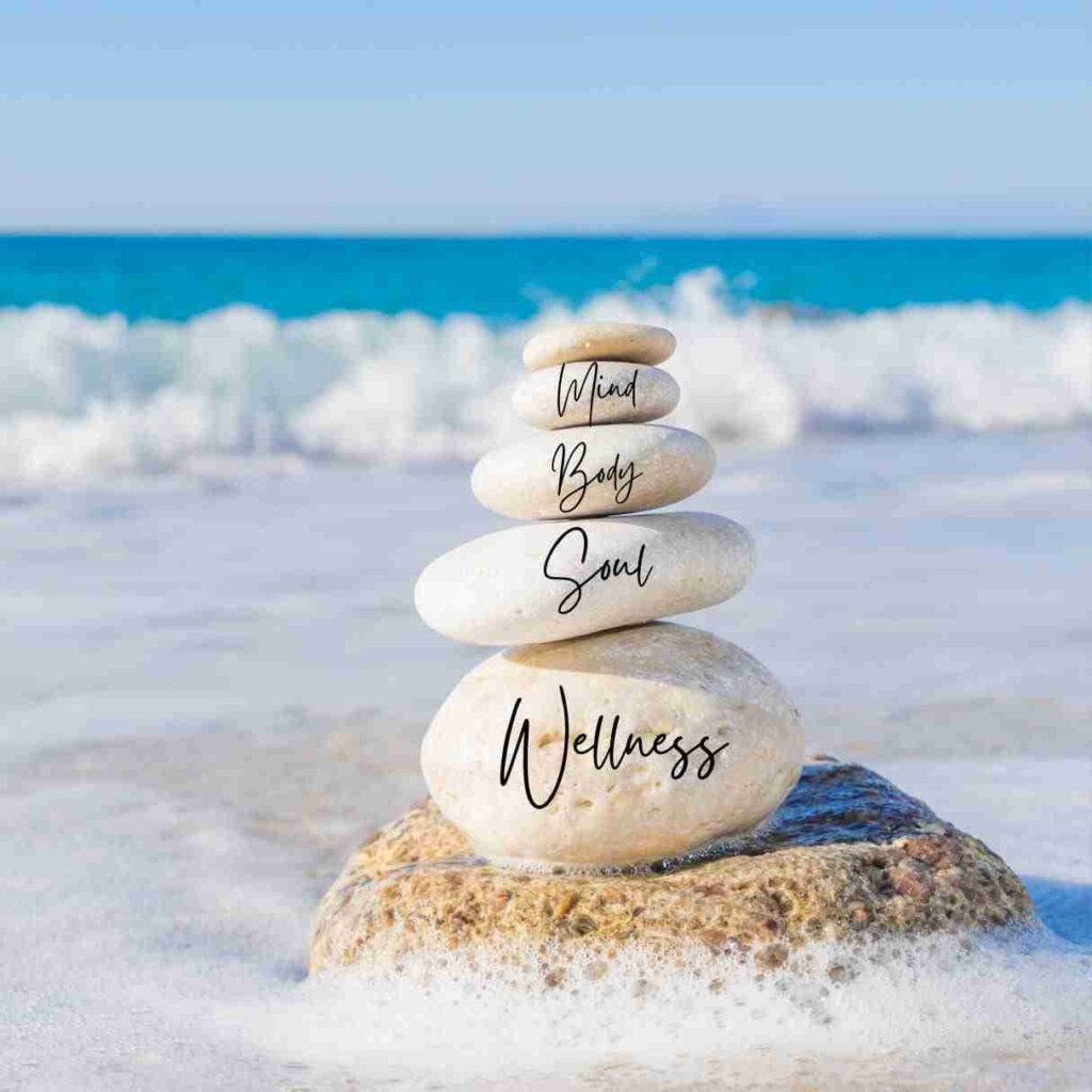 A rock tower on the beach with the words Mind, Body, Soul, and Wellness written on each rock, representing wellness quotes.
