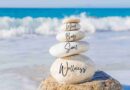 A rock tower on the beach with the words Mind, Body, Soul, and Wellness written on each rock, representing wellness quotes.