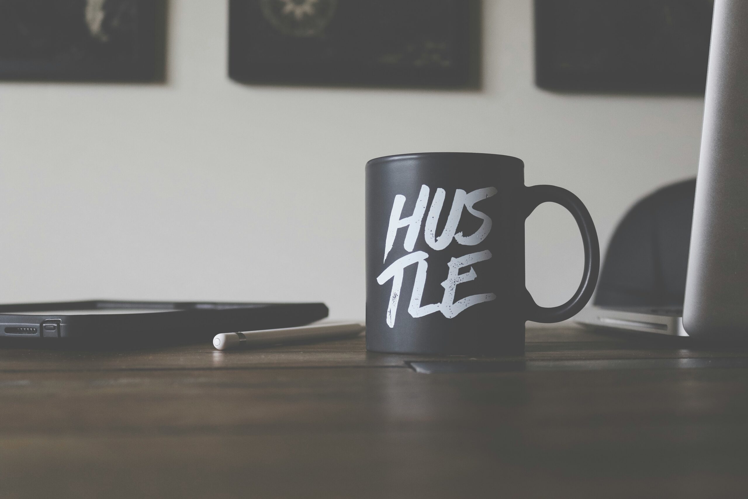 A mug sitting on a desk with the word HUSTLE on it. Alluding to the entrepreneurial struggles one will face on their path.