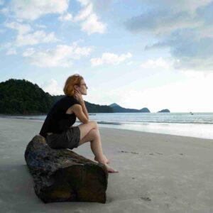 Photo of woman sitting on log on a beach looking pensive. Image by Engin Akyurt from Pixabay