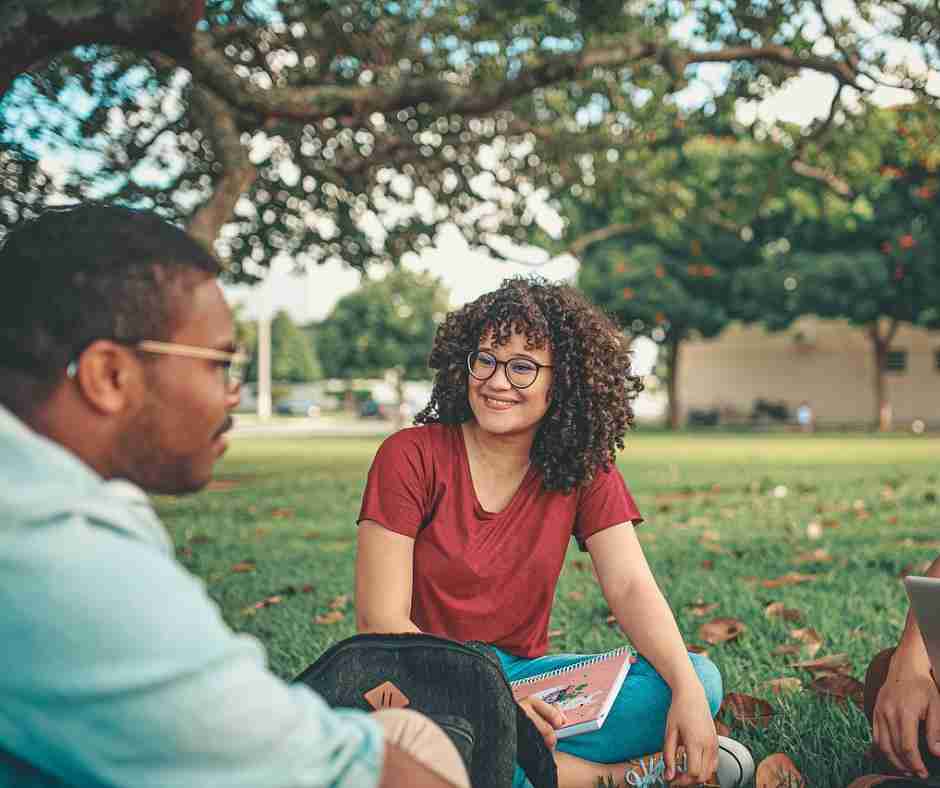Photo of friends/students sitting on grass talking.