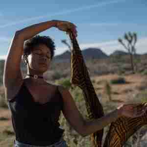 - Resilient Stories Black woman dancing in desert with scarf.