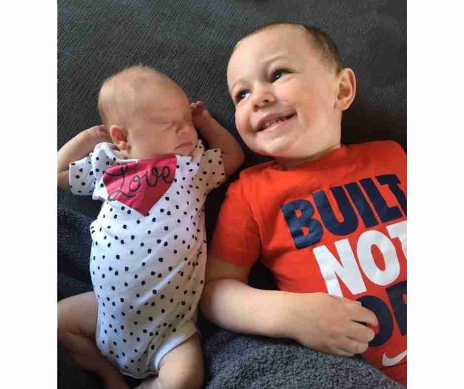 Young boy and his newborn baby sister lying on couch.