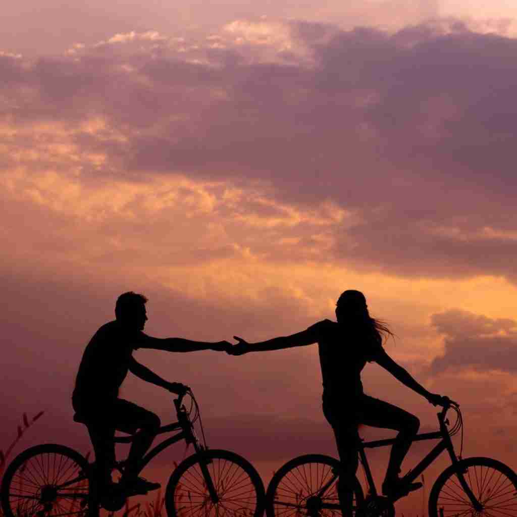 Untitled design (11) - Resilient Stories Photo of couple on bicycles silhouetted against sunset sky.