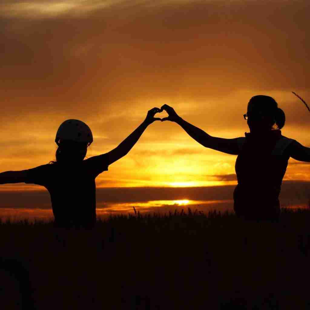 Untitled design (13) - Resilient Stories Photo of mother and child silhouetted against setting sun, connecting their hands in a heart shape