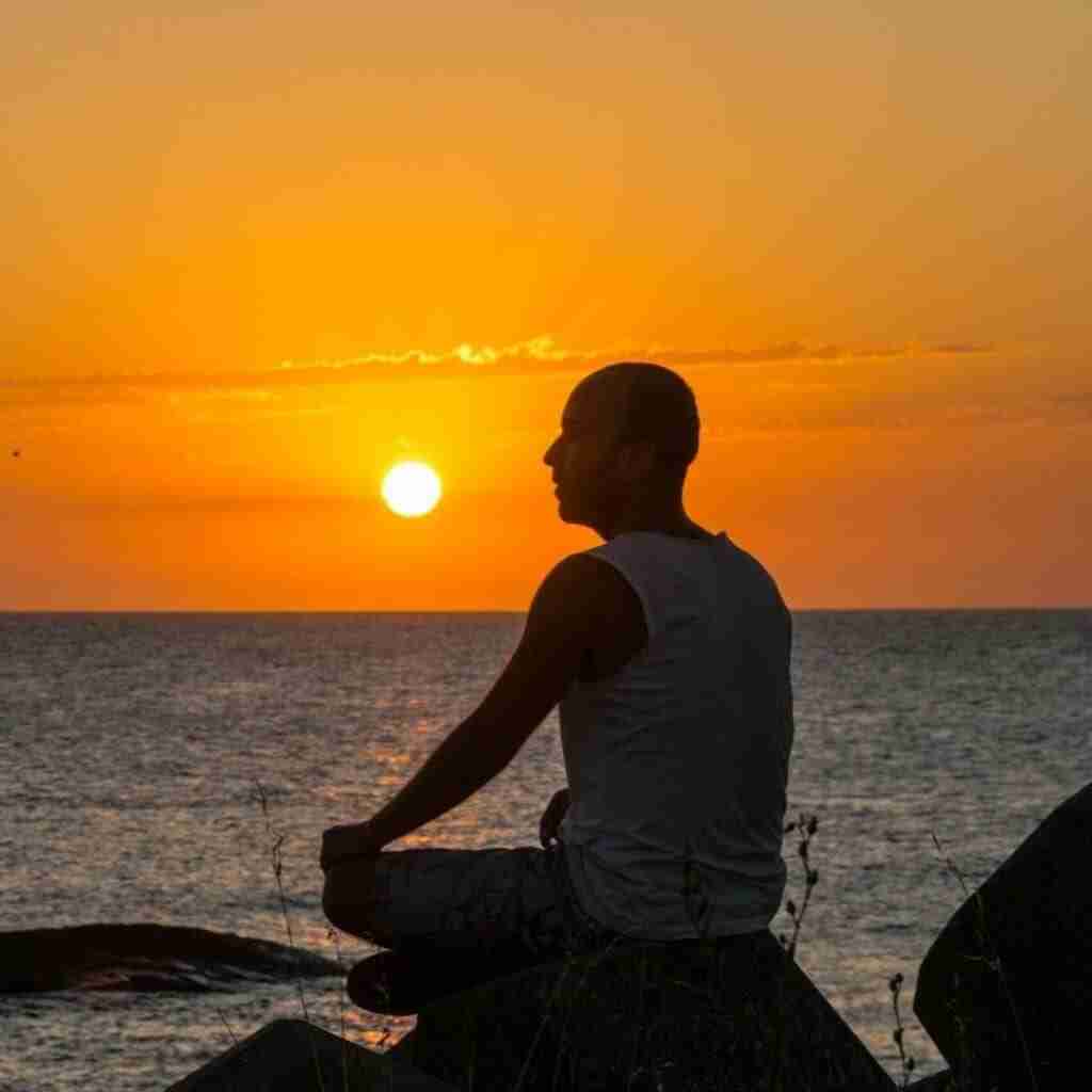7 - Resilient Stories Photo of a man sitting on a rock in front of the ocean and a orange sunset