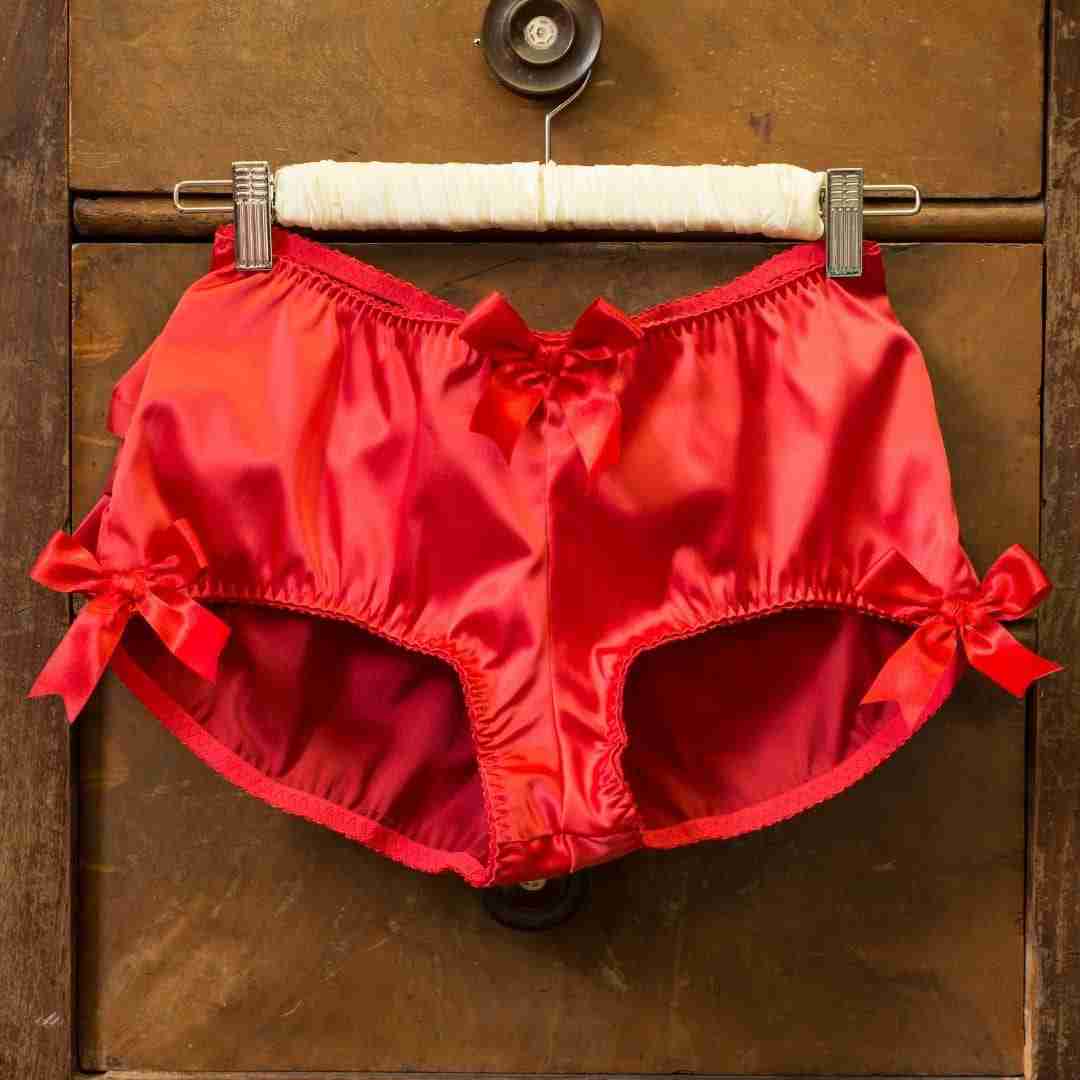 Photo of red underwear hanging on a hanger on a brown dresser drawer.