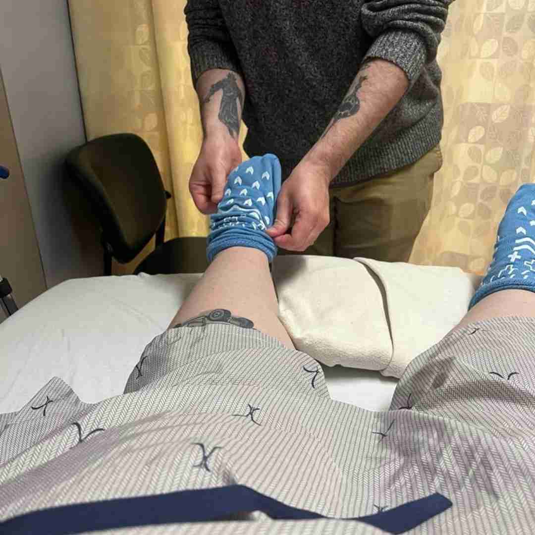 Photo of Keri in hospital, husband putting a sock on her foot.