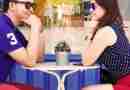 An Asian couple sits at an outdoor cafe gazing and smiling at each other.