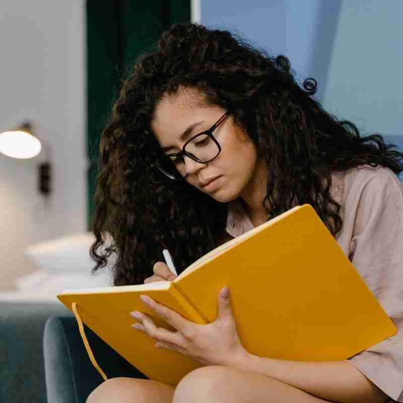 A woman of color writes in a bright gold journal.