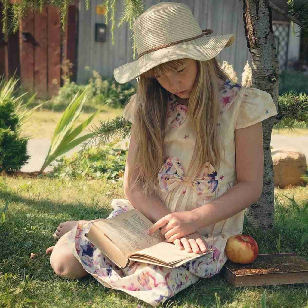 A young girl sits in the grass reading a book demonstrating bibliotherapy.